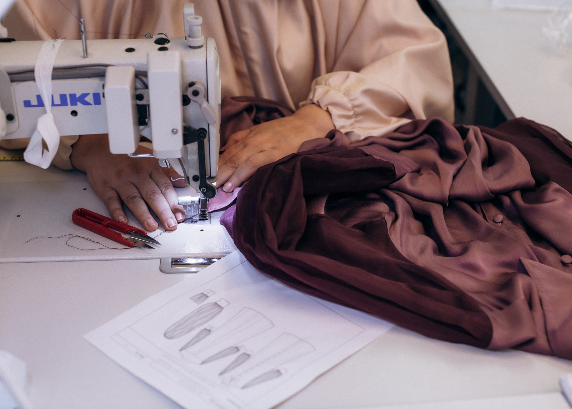 Machinist sewing a satin garment beside its technical drawing at CMT Studio London