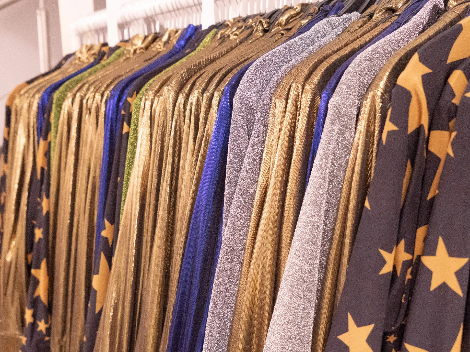 Rail of eveningwear garments on gold hangers, including navy star-print, silver lurex, royal blue and gold pleated fabrics, at CMT Studio London