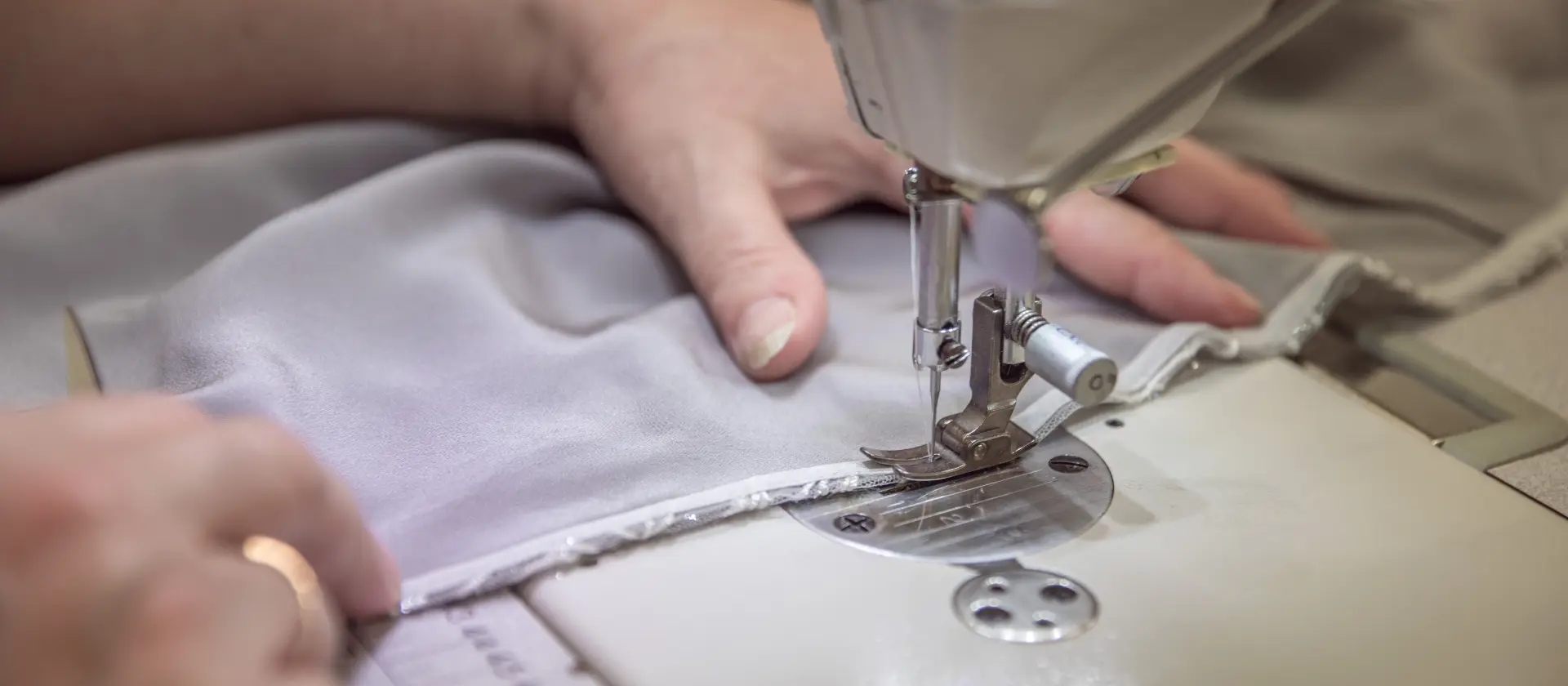 Hands guiding pale fabric under a sewing machine needle at CMT Studio London