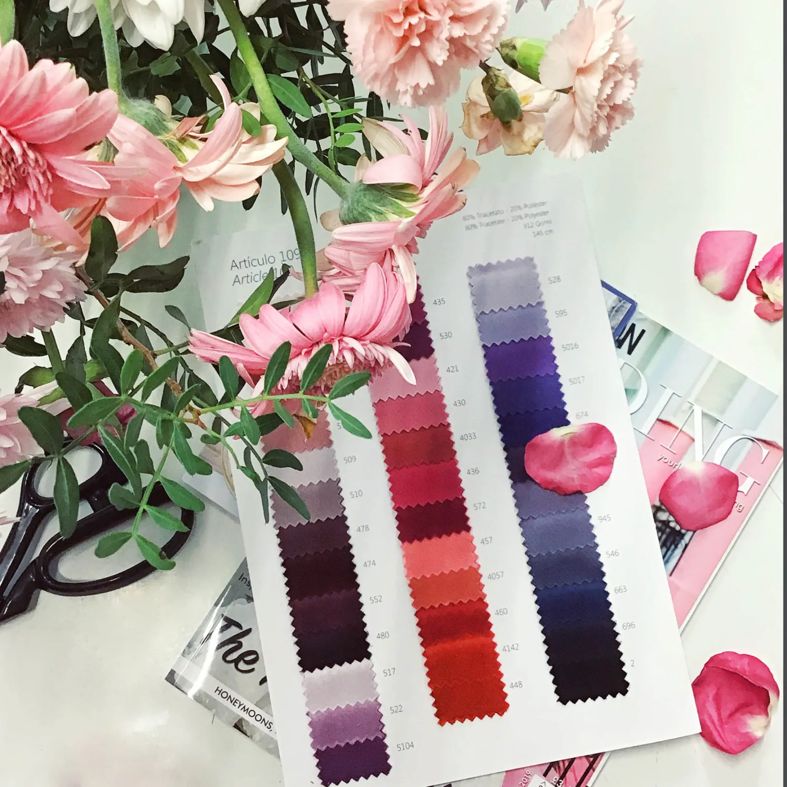 Colour card of satin swatches in purples and reds beside pink flowers and shears at CMT Studio London