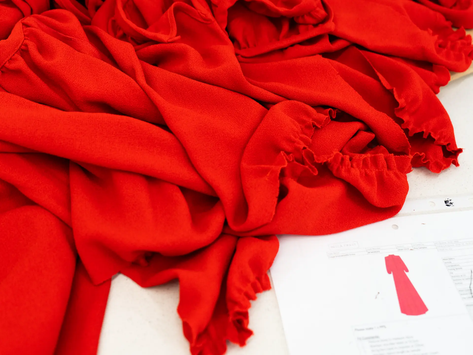 Red garment pieces laid out beside a technical drawing at CMT Studio London