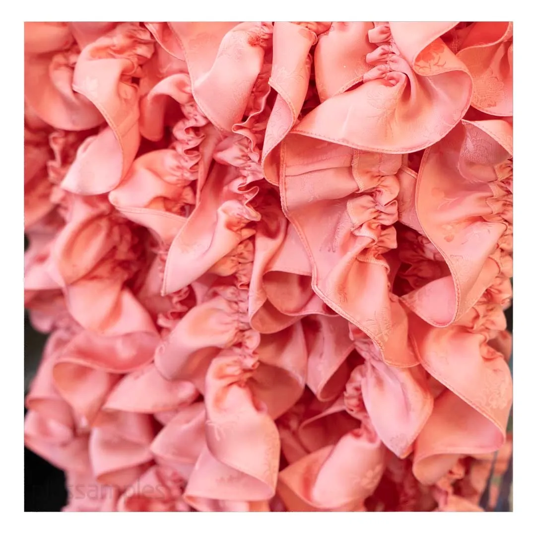 Close-up of cascading coral satin ruffles on a finished evening garment at CMT Studio London