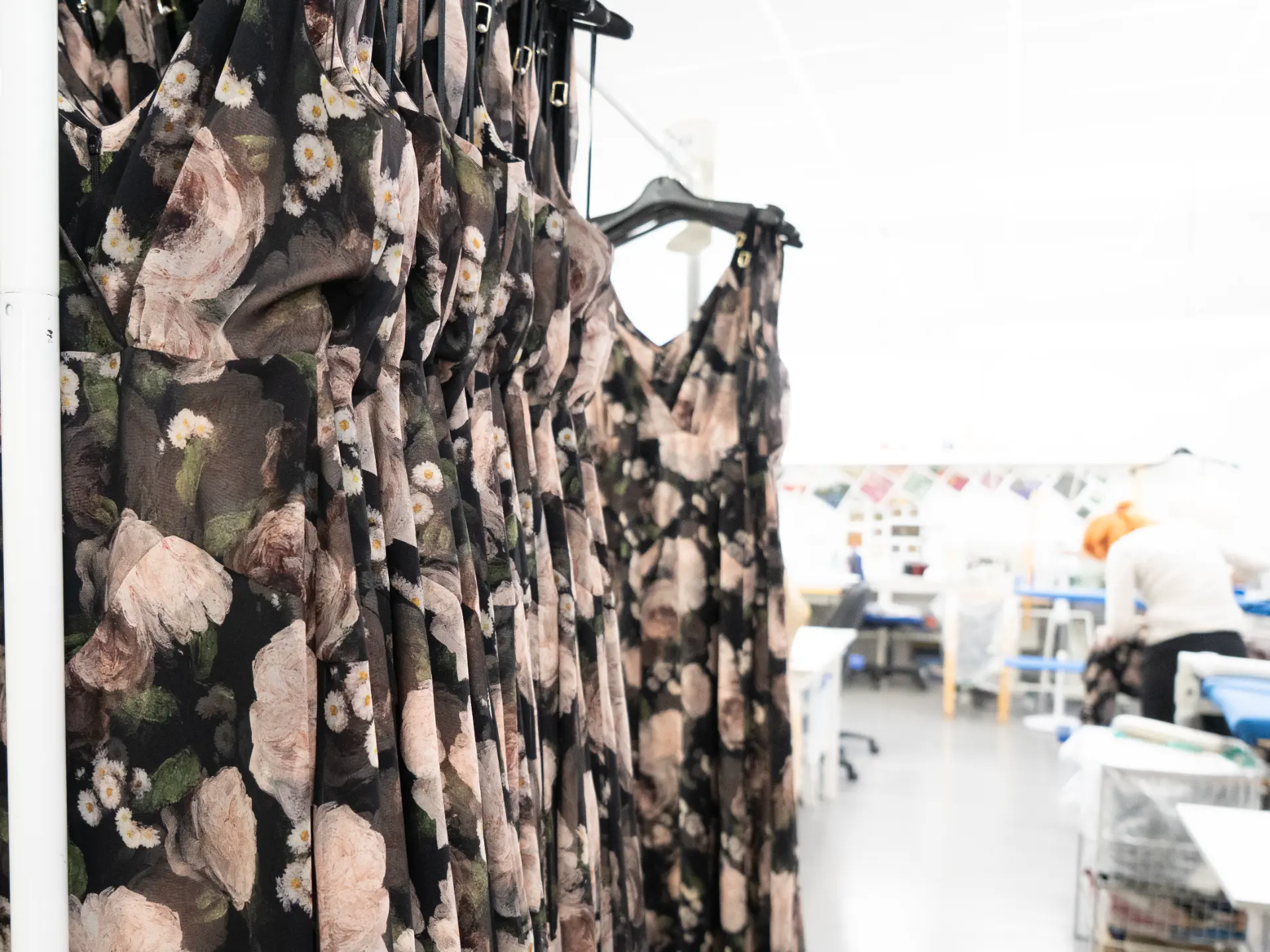 Rail of dark floral evening dresses on white hangers in the studio workroom at CMT Studio London