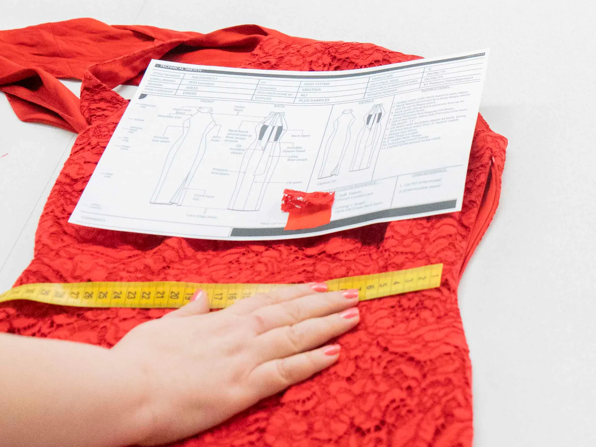 Technical sheet and measuring tape laid over red lace fabric at CMT Studio London