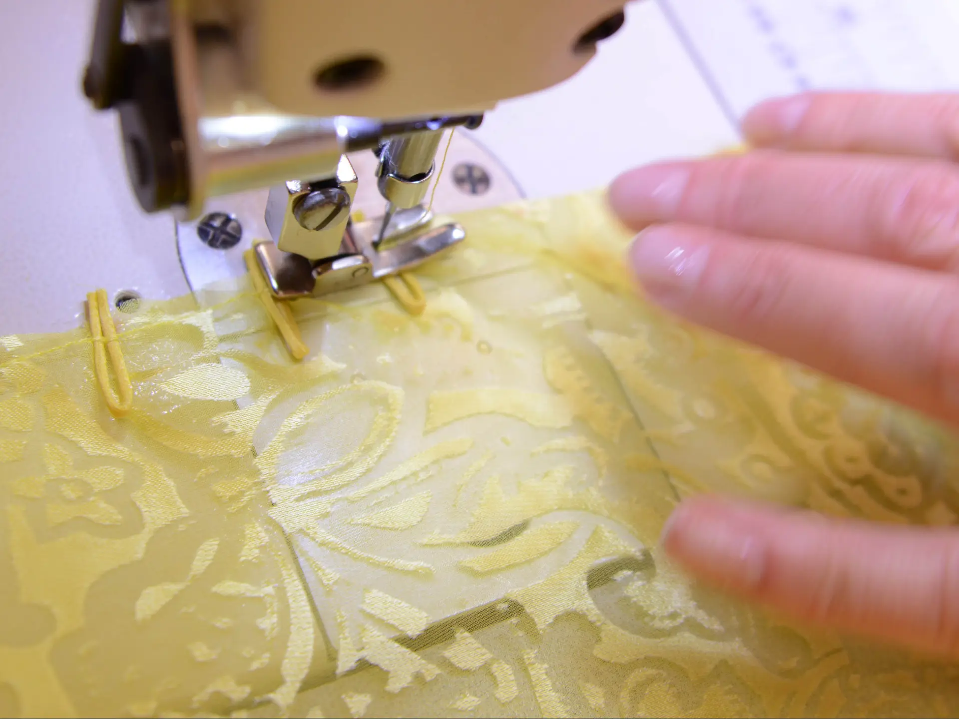 Close view of pale gold patterned silk being stitched under a machine foot