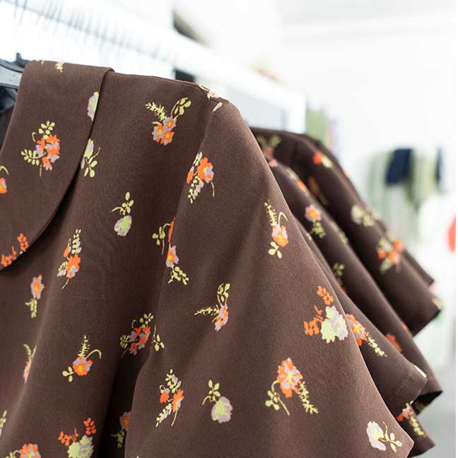 Finished dark floral garments hanging on a rail in the studio, ready for collection