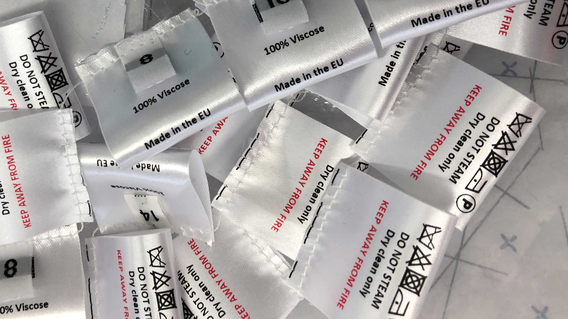 A pile of white satin garment care and composition labels showing fabric content, care symbols and size markings